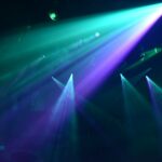 Bright teal and purple spotlights cutting through a dark hazy nightclub atmosphere
