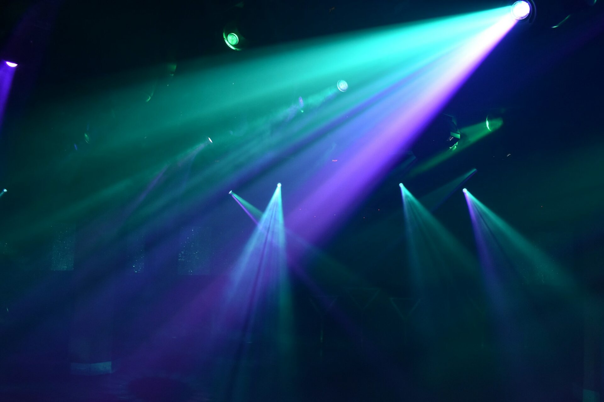 Bright teal and purple spotlights cutting through a dark hazy nightclub atmosphere