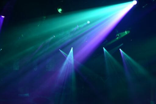 Bright teal and purple spotlights cutting through a dark hazy nightclub atmosphere