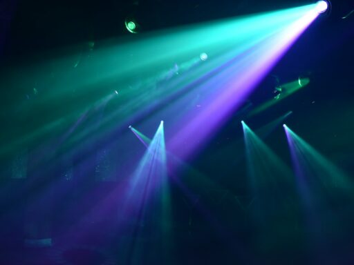 Bright teal and purple spotlights cutting through a dark hazy nightclub atmosphere