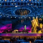 A performer plays piano on a brightly lit stage