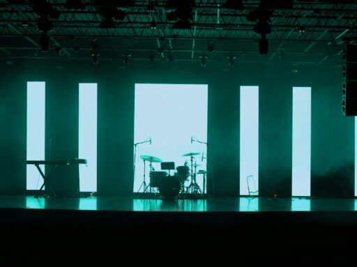 An empty stage with a drum kit and a keyboard in front of tall lit panels.