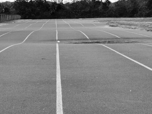 An empty running track with white lane markings and trees behind it.