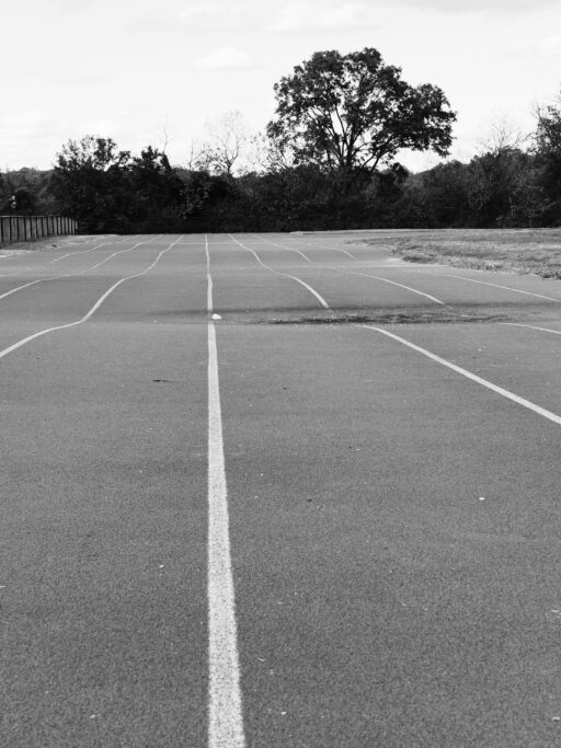 An empty running track with white lane markings and trees behind it.