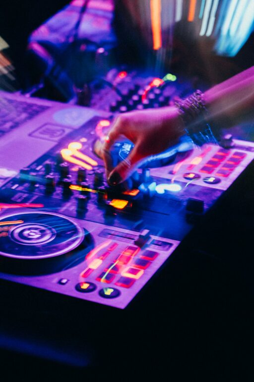 A hand on a lit DJ controller in purple and orange light, with motion blur.