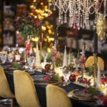 A holiday dinner table set with candles, gold chairs and warm lights.