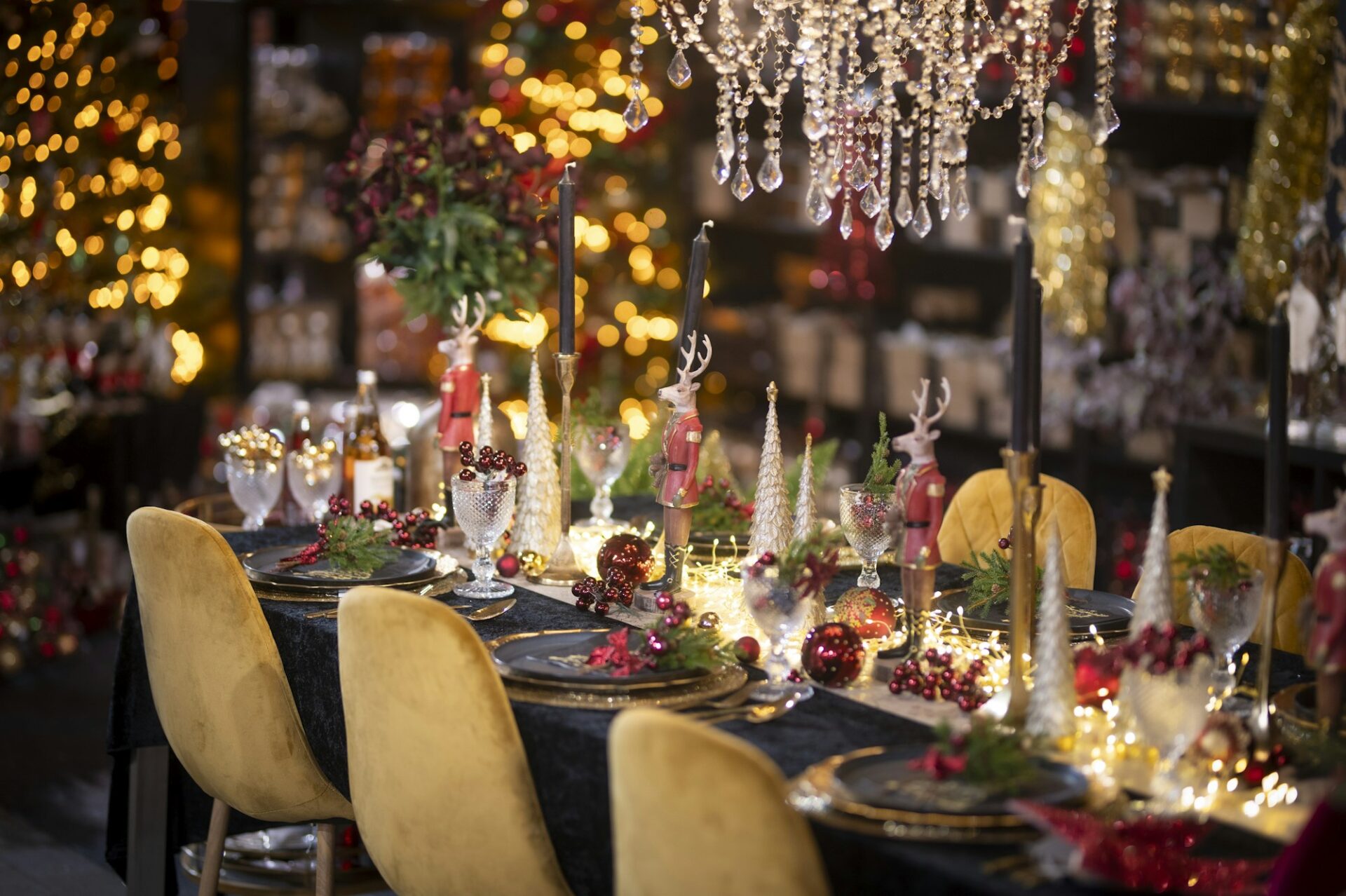 A holiday dinner table set with candles, gold chairs and warm lights.