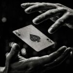 Two hands with an ace of spades playing card floating between them, in black and white, with soft lights behind.