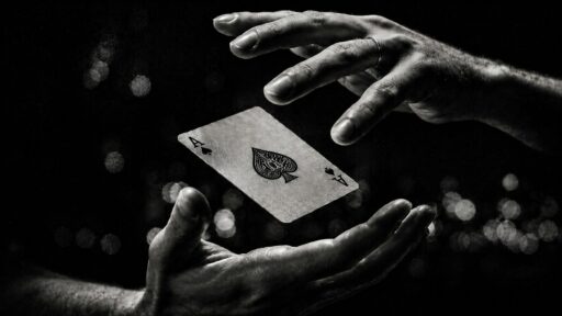 Two hands with an ace of spades playing card floating between them, in black and white, with soft lights behind.