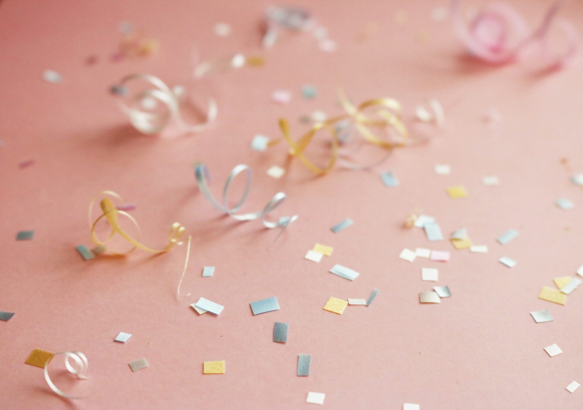 Curled ribbons and pastel confetti on a pink surface.