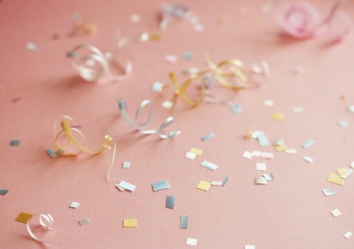 Curled ribbons and pastel confetti on a pink surface.