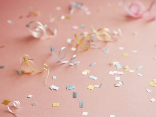Curled ribbons and pastel confetti on a pink surface.