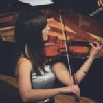 Woman playing violin beside a grand piano