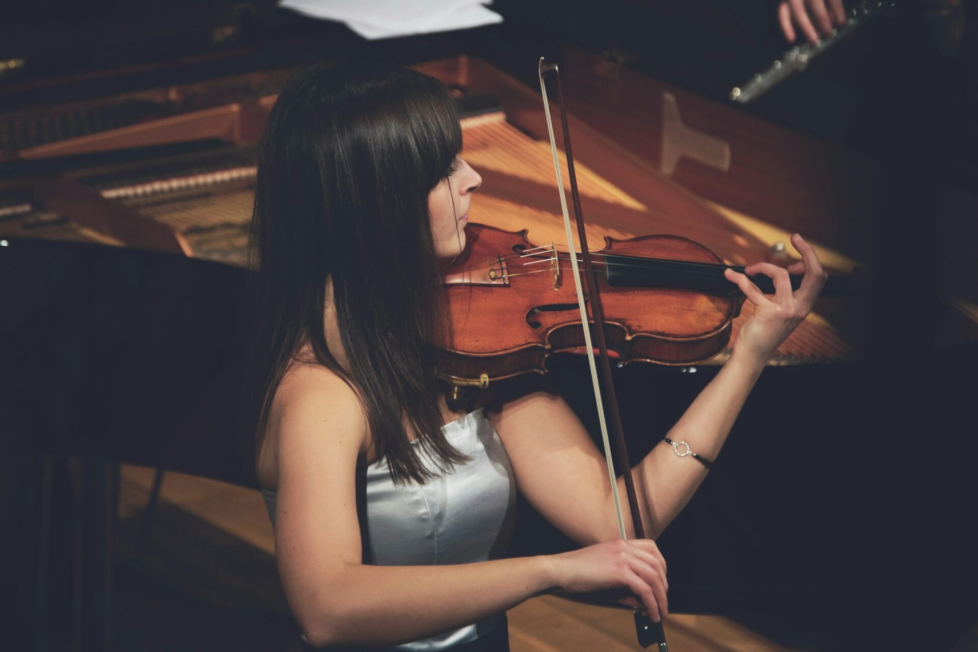 Woman playing violin beside a grand piano