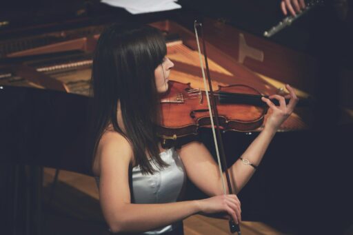 Woman playing violin beside a grand piano