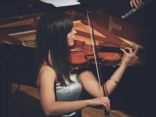 Woman playing violin beside a grand piano