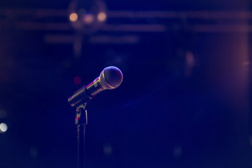A microphone on a stand in front of a blurred, dimly lit stage.