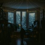 A room lit by fairy lights, with snowy trees outside the windows.