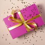 A pink gift box tied with a gold ribbon, with small gold hearts scattered around it.