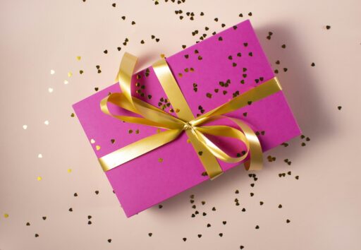 A pink gift box tied with a gold ribbon, with small gold hearts scattered around it.