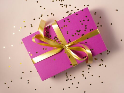 A pink gift box tied with a gold ribbon, with small gold hearts scattered around it.