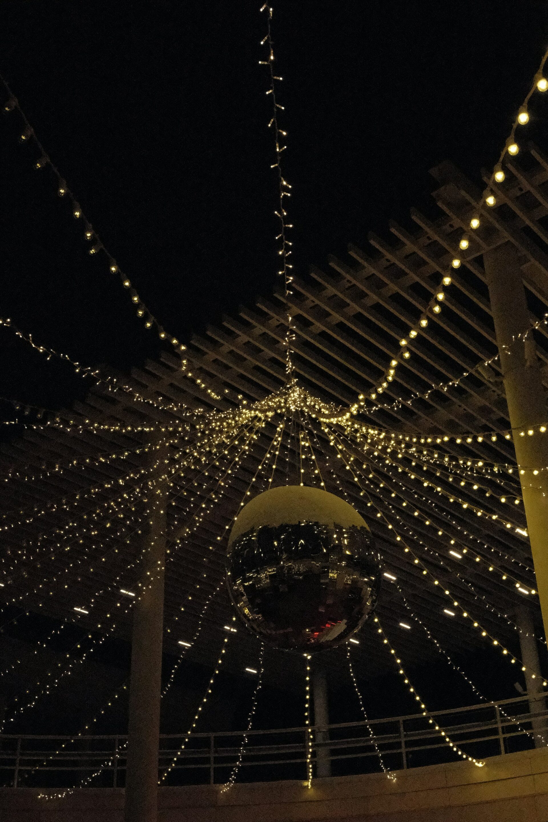 A mirror ball hanging under strings of fairy lights on a covered terrace at night.
