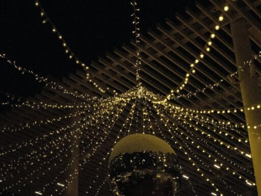 A mirror ball hanging under strings of fairy lights on a covered terrace at night.