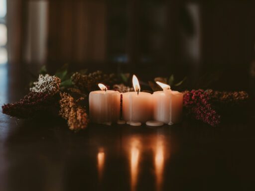Three lit white candles among dried flowers on a dark wooden table.