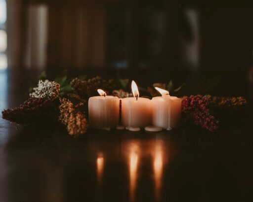 Three lit white candles among dried flowers on a dark wooden table.