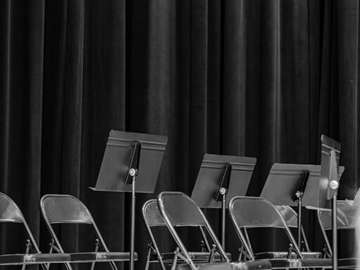 Empty folding chairs and music stands on a stage in front of a dark curtain.