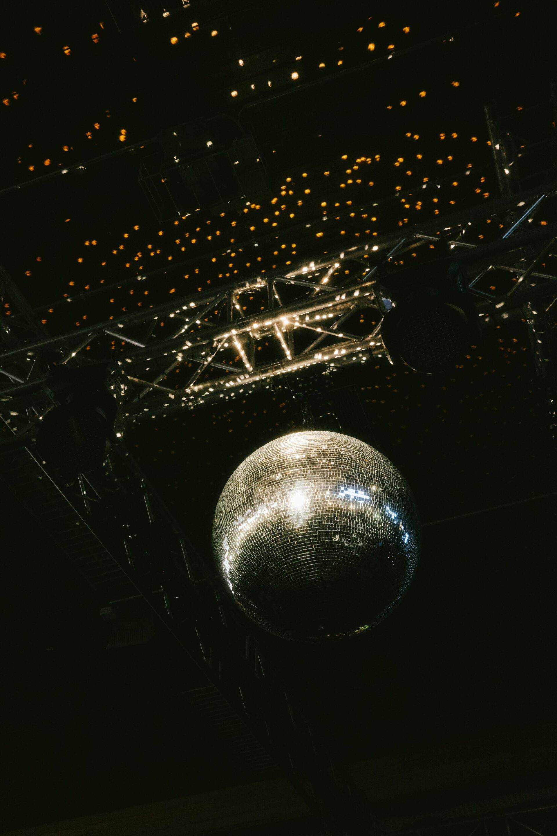 A mirror ball hanging from a lighting rig under a ceiling of small warm lights.