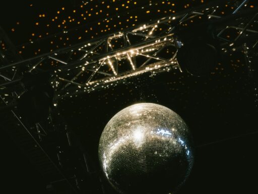 A mirror ball hanging from a lighting rig under a ceiling of small warm lights.