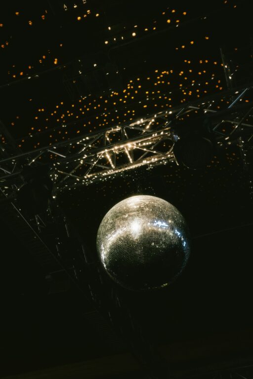 A mirror ball hanging from a lighting rig under a ceiling of small warm lights.