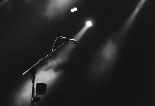 A microphone on a stand under a spotlight on a dark, foggy stage.