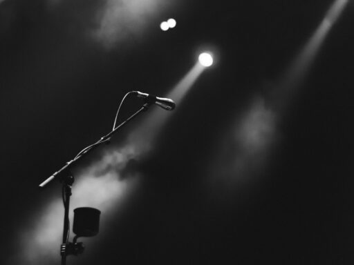 A microphone on a stand under a spotlight on a dark, foggy stage.