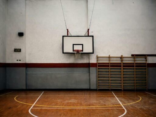 An empty school gym with a basketball hoop and wall bars.