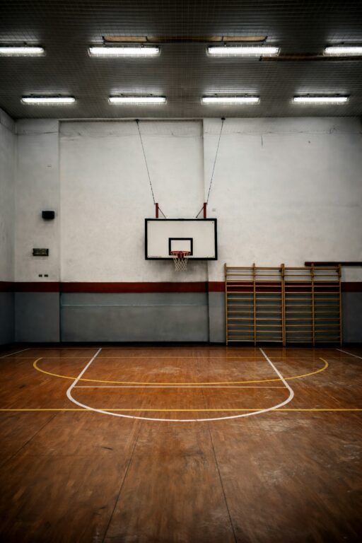 An empty school gym with a basketball hoop and wall bars.