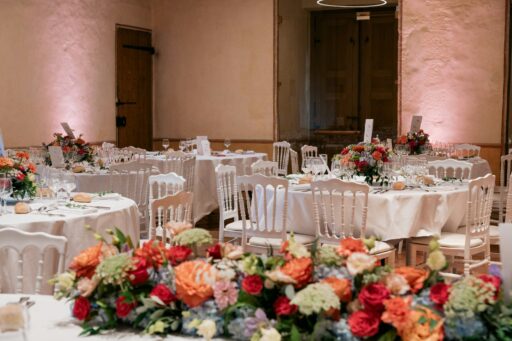 Round reception tables with white chairs and bright flower centrepieces.