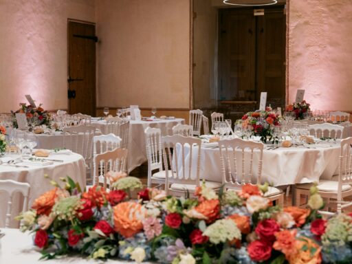 Round reception tables with white chairs and bright flower centrepieces.