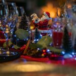 A holiday table with candles, glasses and a Santa figurine.