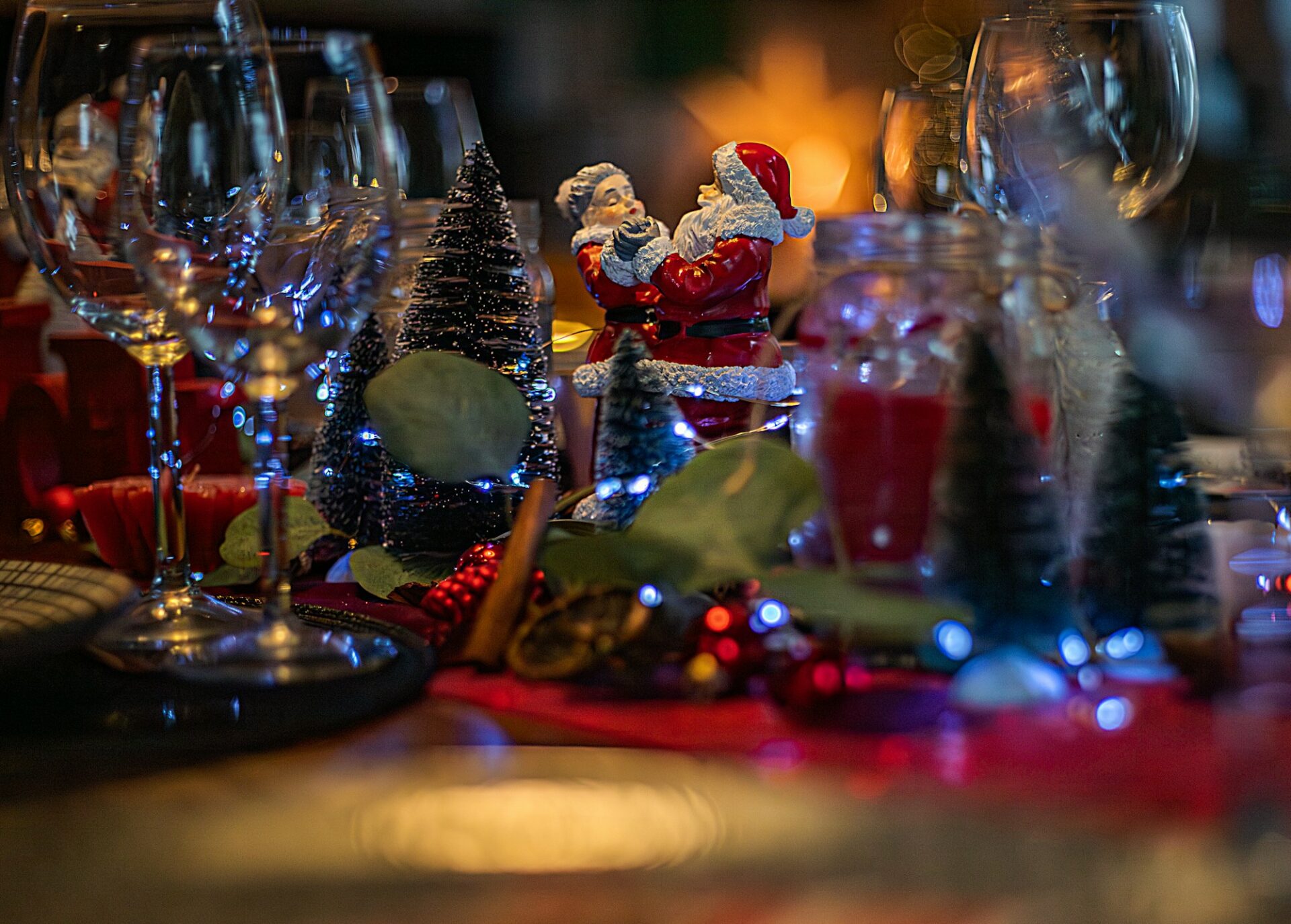 A holiday table with candles, glasses and a Santa figurine.