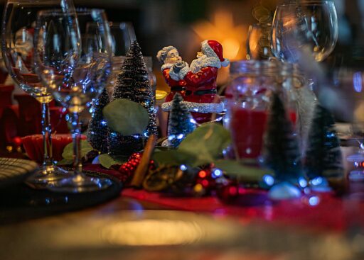 A holiday table with candles, glasses and a Santa figurine.