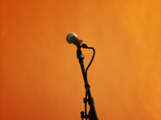 A microphone on a stand against a bright orange wall.