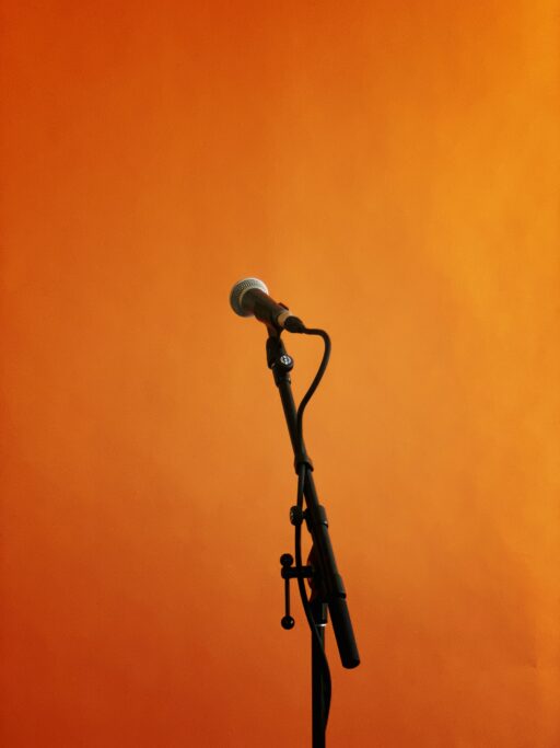A microphone on a stand against a bright orange wall.